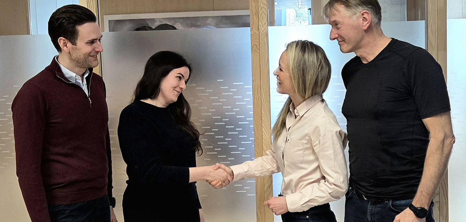 Bildet synes fire mennske som inngår ein kontrakt og hilser kvarandre i handa