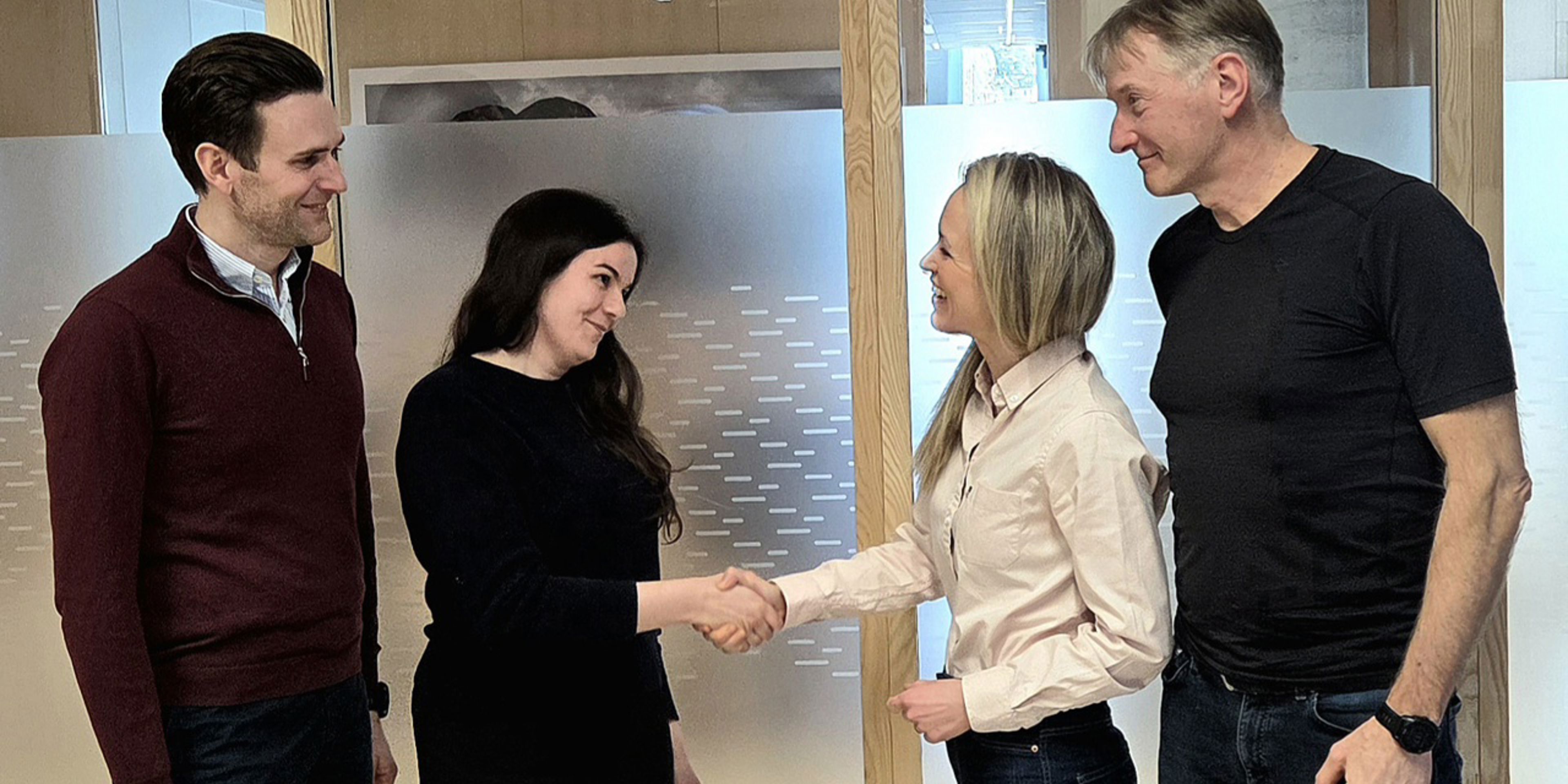 Bildet synes fire mennske som inngår ein kontrakt og hilser kvarandre i handa